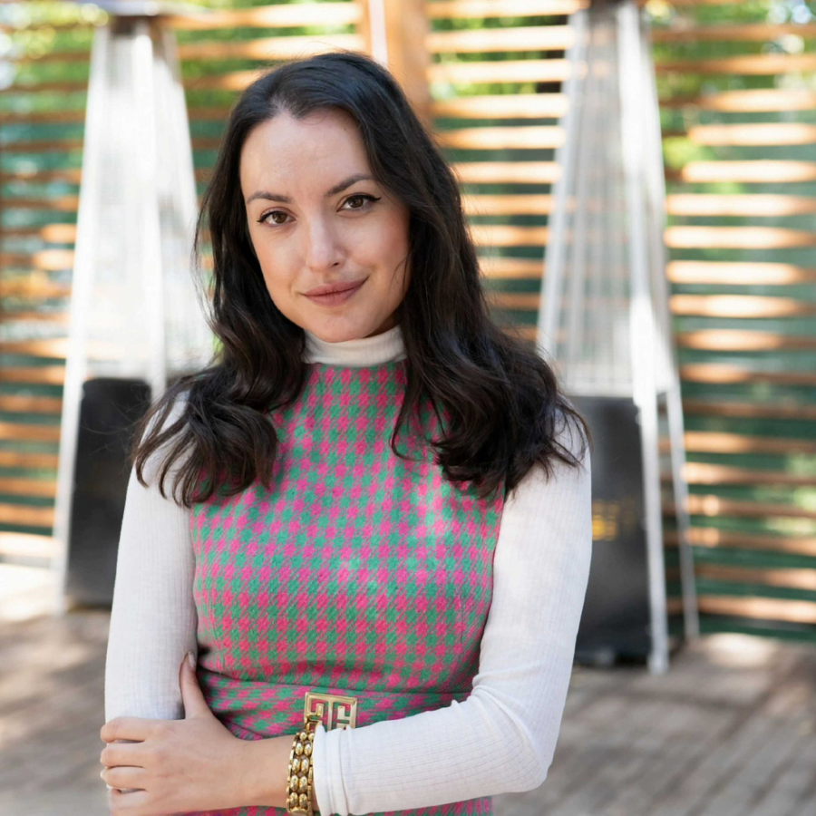 A headshot of a girl with dark hair and wearing a top with white long sleeves, and a square green-pink pattern.